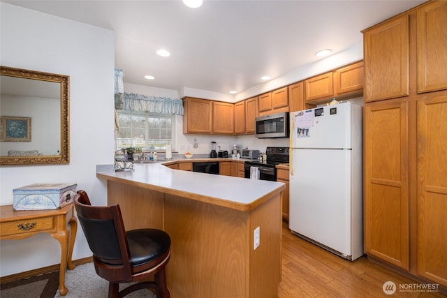 kitchen featuring stainless steel microwave, electric range, brown cabinetry, freestanding refrigerator, and a peninsula