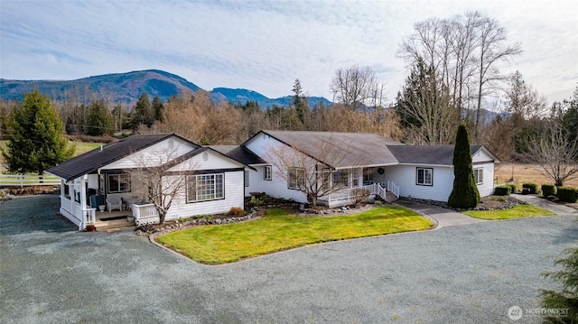 ranch-style home featuring driveway, covered porch, a mountain view, and a front lawn