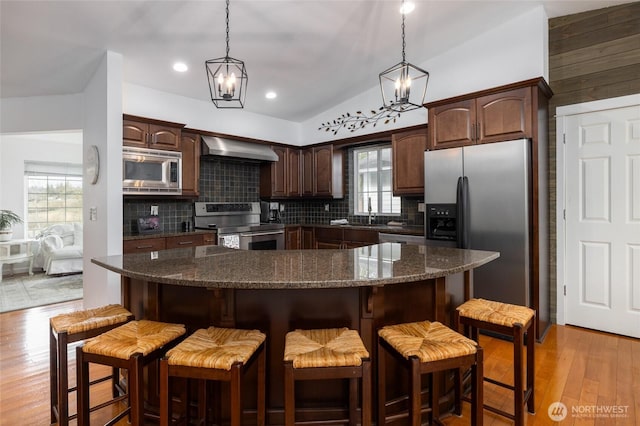 kitchen with light wood-type flooring, wall chimney range hood, tasteful backsplash, and stainless steel appliances