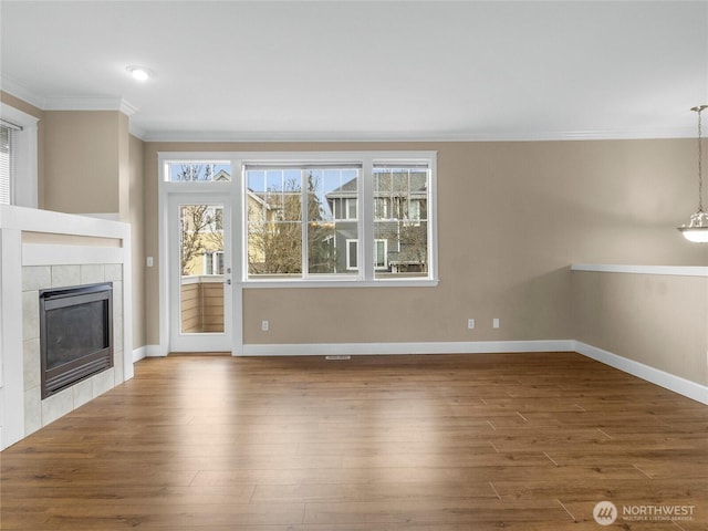 unfurnished living room with baseboards, a tiled fireplace, wood finished floors, and crown molding