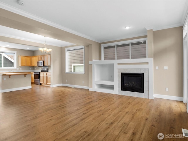 unfurnished living room with crown molding, a tiled fireplace, an inviting chandelier, light wood-style floors, and baseboards