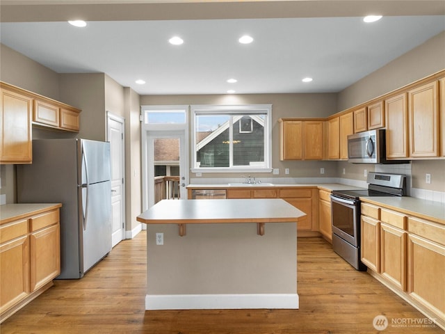 kitchen with a kitchen island, stainless steel appliances, light countertops, light wood-style floors, and a sink