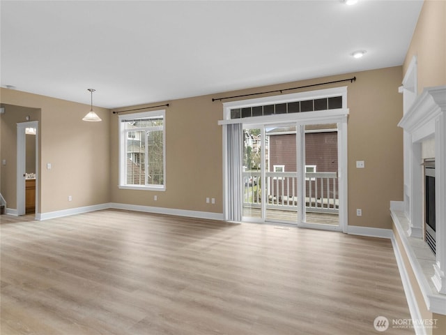 unfurnished living room featuring light wood finished floors, baseboards, and a fireplace with raised hearth