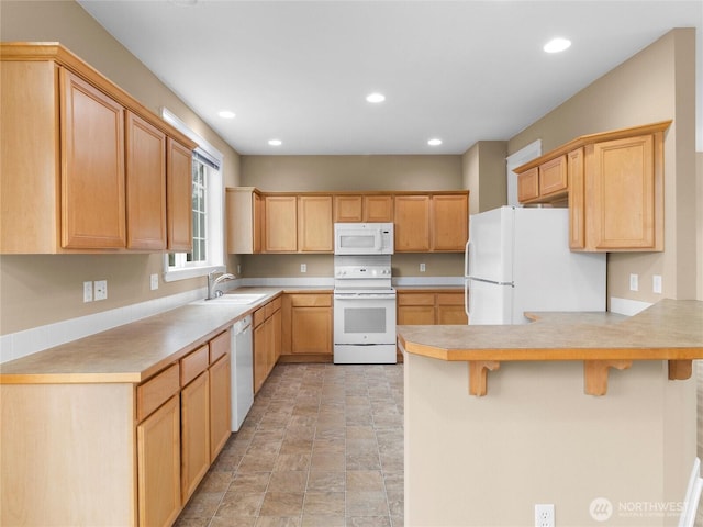 kitchen featuring white appliances, a breakfast bar area, light countertops, light brown cabinetry, and a sink