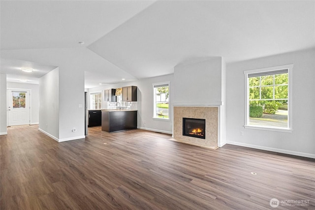 unfurnished living room featuring lofted ceiling, dark wood-style flooring, a tiled fireplace, and baseboards