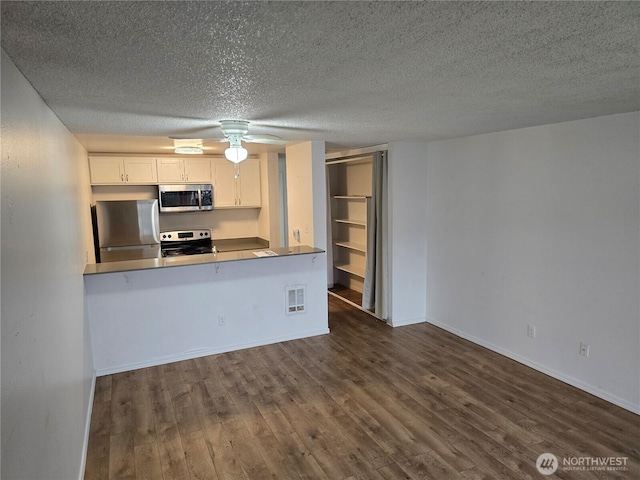 kitchen featuring visible vents, dark wood-style flooring, a peninsula, stainless steel appliances, and white cabinetry