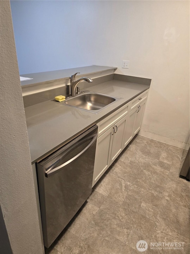 kitchen with baseboards, dark countertops, stainless steel dishwasher, white cabinetry, and a sink