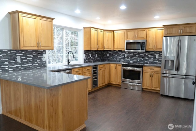 kitchen featuring wine cooler, a peninsula, dark wood-type flooring, a sink, and appliances with stainless steel finishes