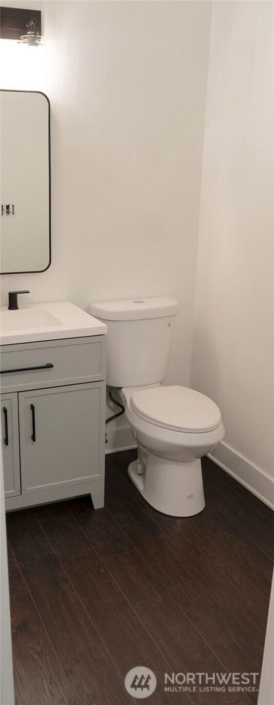 bathroom featuring toilet, baseboards, wood finished floors, and vanity