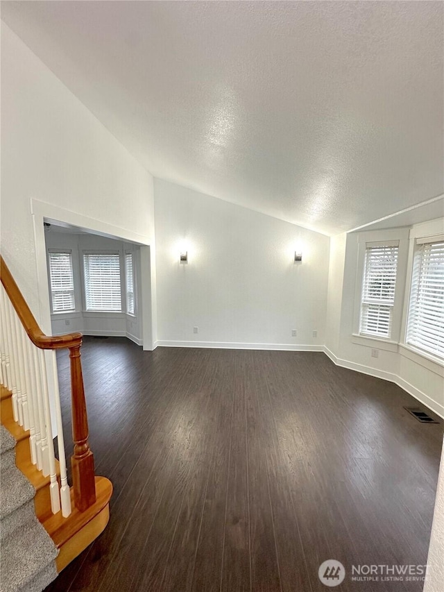 unfurnished living room with lofted ceiling, dark wood-type flooring, a textured ceiling, baseboards, and stairs