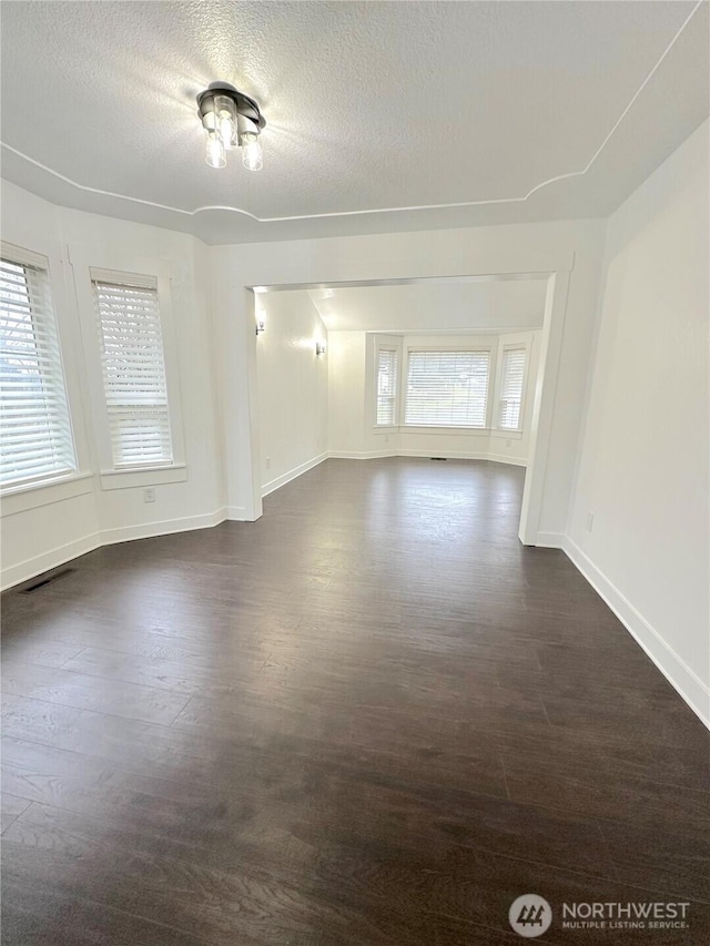 unfurnished room featuring dark wood-style floors, a textured ceiling, visible vents, and baseboards