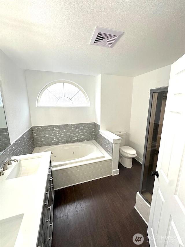 full bath featuring visible vents, toilet, a sink, wood finished floors, and a whirlpool tub