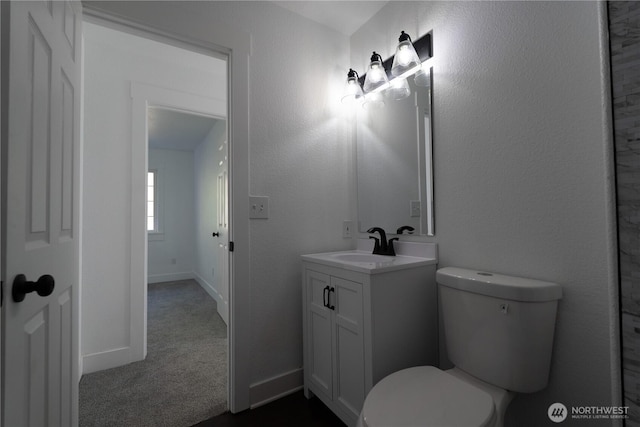 bathroom featuring baseboards, a textured wall, vanity, and toilet