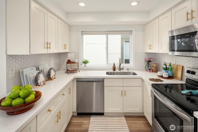 kitchen featuring wood finished floors, appliances with stainless steel finishes, a sink, and white cabinetry