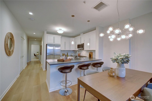 kitchen with stainless steel appliances, dark countertops, visible vents, decorative backsplash, and white cabinets