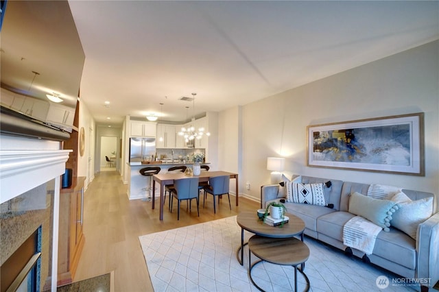 living area featuring visible vents, baseboards, a premium fireplace, light wood-type flooring, and a notable chandelier