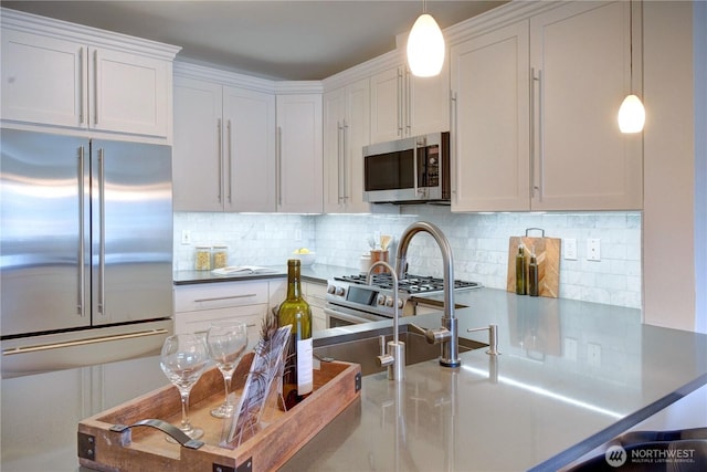 kitchen with a sink, white cabinets, appliances with stainless steel finishes, tasteful backsplash, and decorative light fixtures