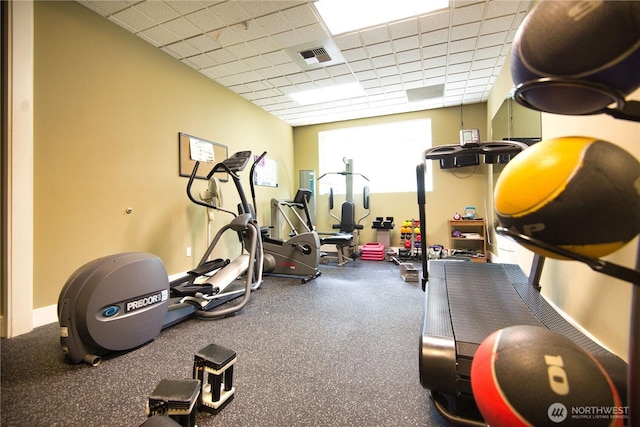 exercise room featuring visible vents, a paneled ceiling, and baseboards