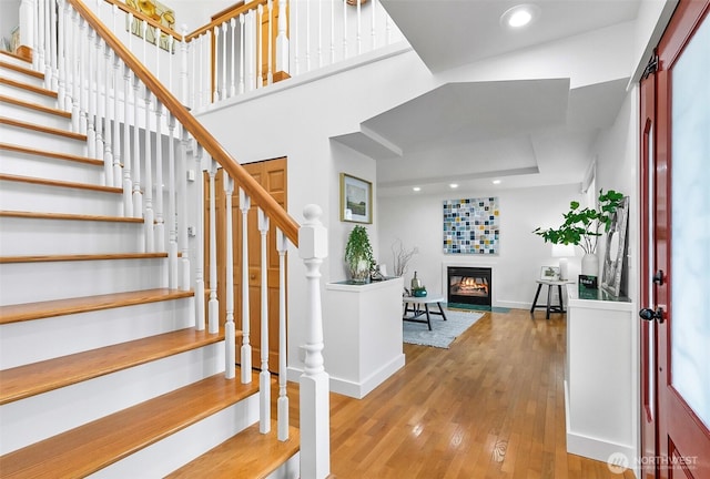 foyer entrance with a glass covered fireplace, recessed lighting, stairway, wood-type flooring, and baseboards