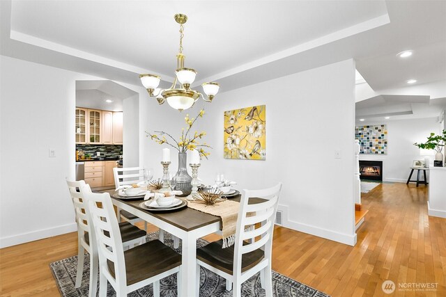 dining room with light wood finished floors, baseboards, recessed lighting, an inviting chandelier, and a glass covered fireplace