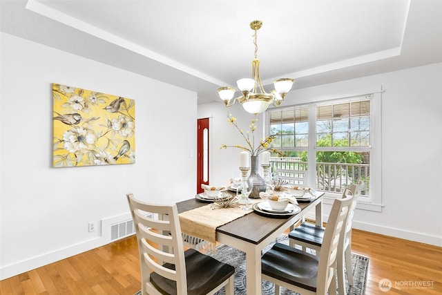 dining space with visible vents, baseboards, wood finished floors, a notable chandelier, and a raised ceiling