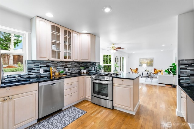 kitchen featuring plenty of natural light, dark countertops, stainless steel appliances, a peninsula, and decorative backsplash