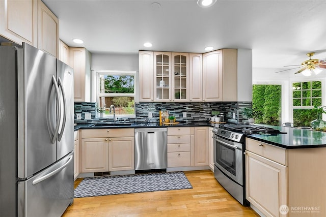 kitchen featuring dark countertops, light wood finished floors, appliances with stainless steel finishes, a peninsula, and a sink