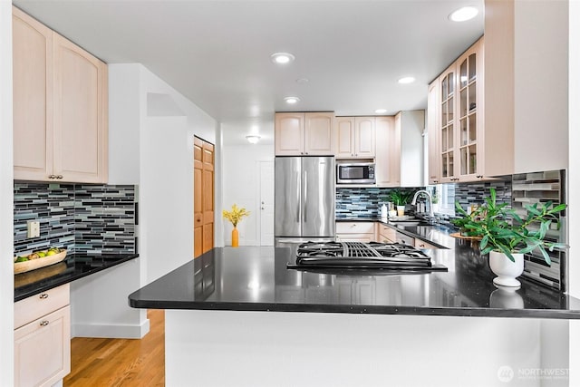 kitchen with a peninsula, a sink, glass insert cabinets, light wood-style floors, and appliances with stainless steel finishes