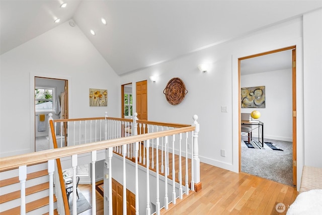 corridor with an upstairs landing, light wood finished floors, high vaulted ceiling, and baseboards