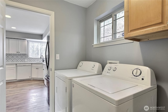 clothes washing area with light wood-style floors, washing machine and dryer, a healthy amount of sunlight, and cabinet space