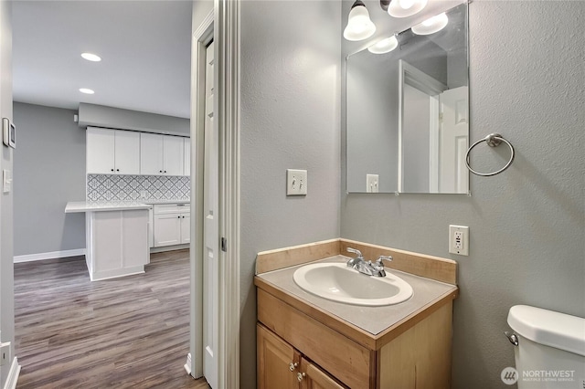 bathroom featuring toilet, recessed lighting, wood finished floors, vanity, and decorative backsplash