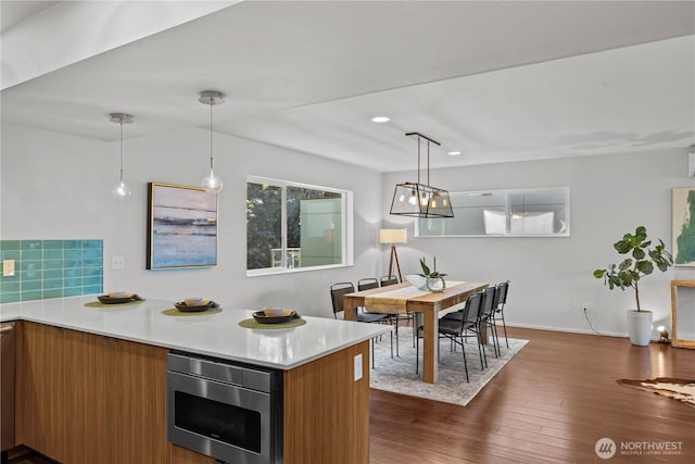 kitchen featuring brown cabinets, light countertops, pendant lighting, and stainless steel microwave