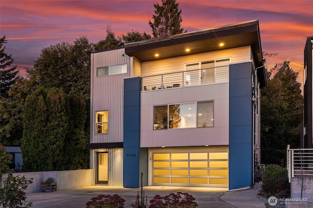 contemporary home with concrete driveway, a balcony, and an attached garage