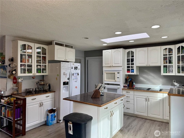 kitchen featuring white appliances, a center island, glass insert cabinets, and white cabinetry