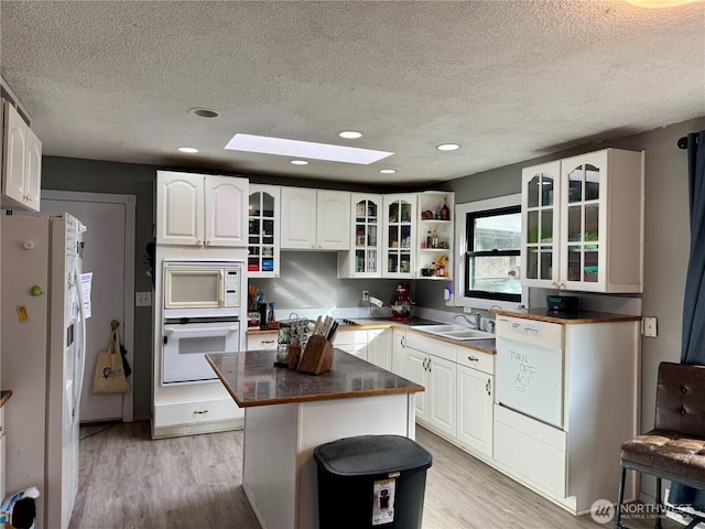 kitchen with white appliances, a sink, a kitchen island, white cabinetry, and glass insert cabinets