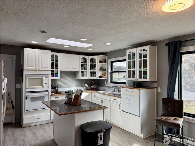 kitchen with white appliances, white cabinets, glass insert cabinets, a center island, and a sink