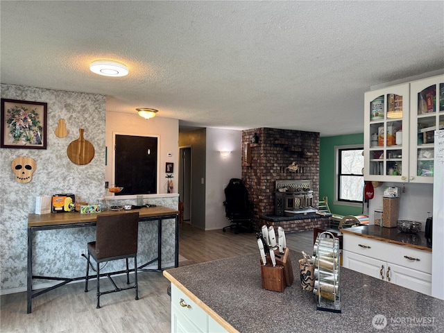 kitchen featuring a textured ceiling, light wood-style floors, white cabinets, dark countertops, and glass insert cabinets