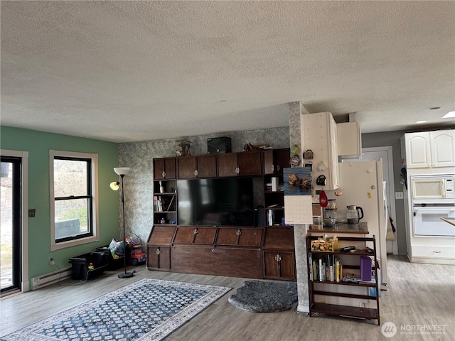 living area with a baseboard heating unit, light wood-type flooring, and baseboards