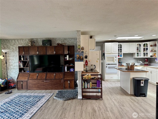 living room featuring light wood-style flooring, a textured ceiling, and wallpapered walls