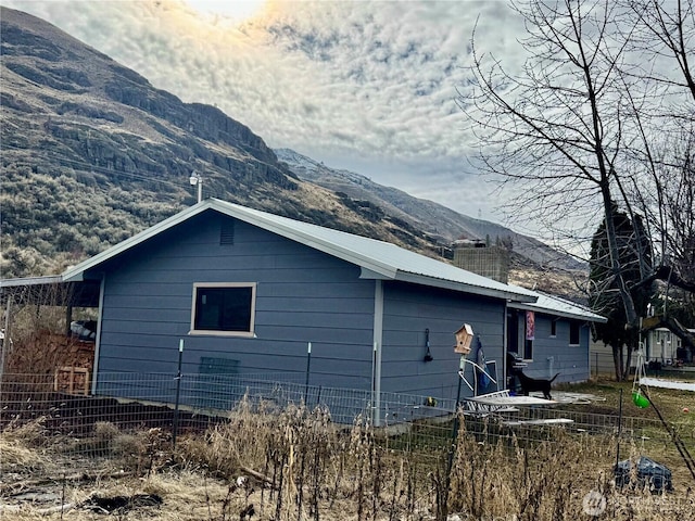 view of home's exterior featuring a chimney, fence, a mountain view, and metal roof