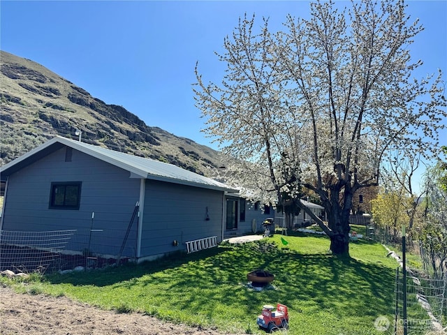 view of side of property with a yard, metal roof, a fire pit, fence, and a mountain view