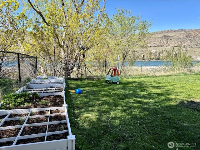view of yard featuring a garden, fence, and a water and mountain view