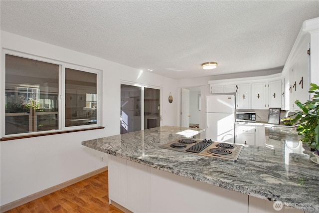 kitchen with light stone counters, freestanding refrigerator, stainless steel microwave, and a peninsula