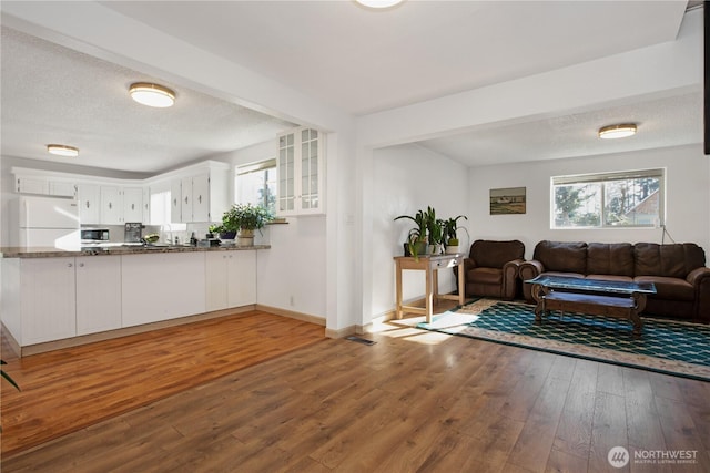 living area with visible vents, a textured ceiling, baseboards, and wood finished floors