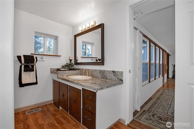 bathroom with visible vents, vanity, baseboards, and wood finished floors