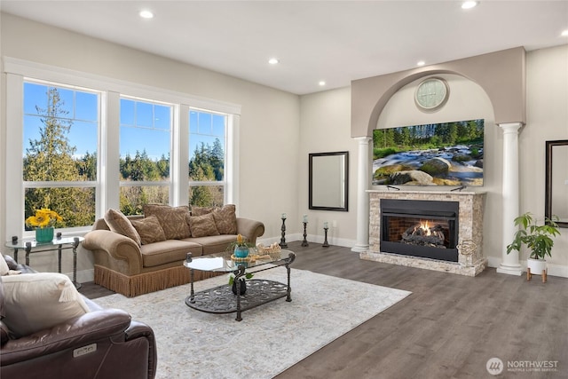 living area with a warm lit fireplace, dark wood-style flooring, decorative columns, and recessed lighting