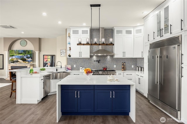 kitchen with stainless steel appliances, light countertops, glass insert cabinets, wall chimney range hood, and a peninsula