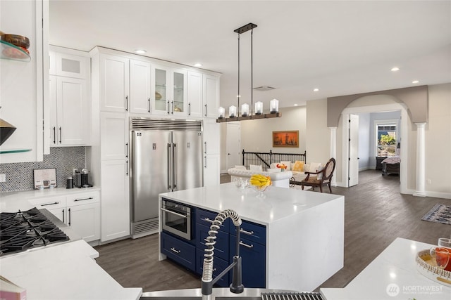 kitchen featuring glass insert cabinets, stainless steel appliances, blue cabinetry, white cabinetry, and pendant lighting