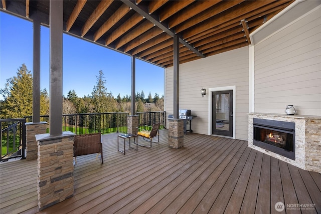 wooden terrace with an outdoor stone fireplace and area for grilling