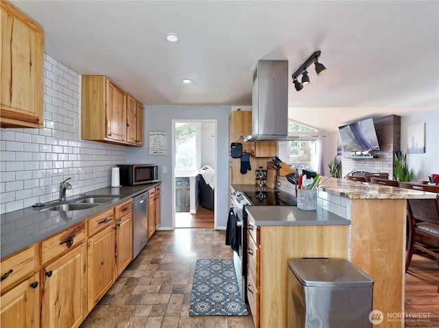 kitchen featuring stone tile floors, island range hood, stainless steel appliances, a sink, and backsplash